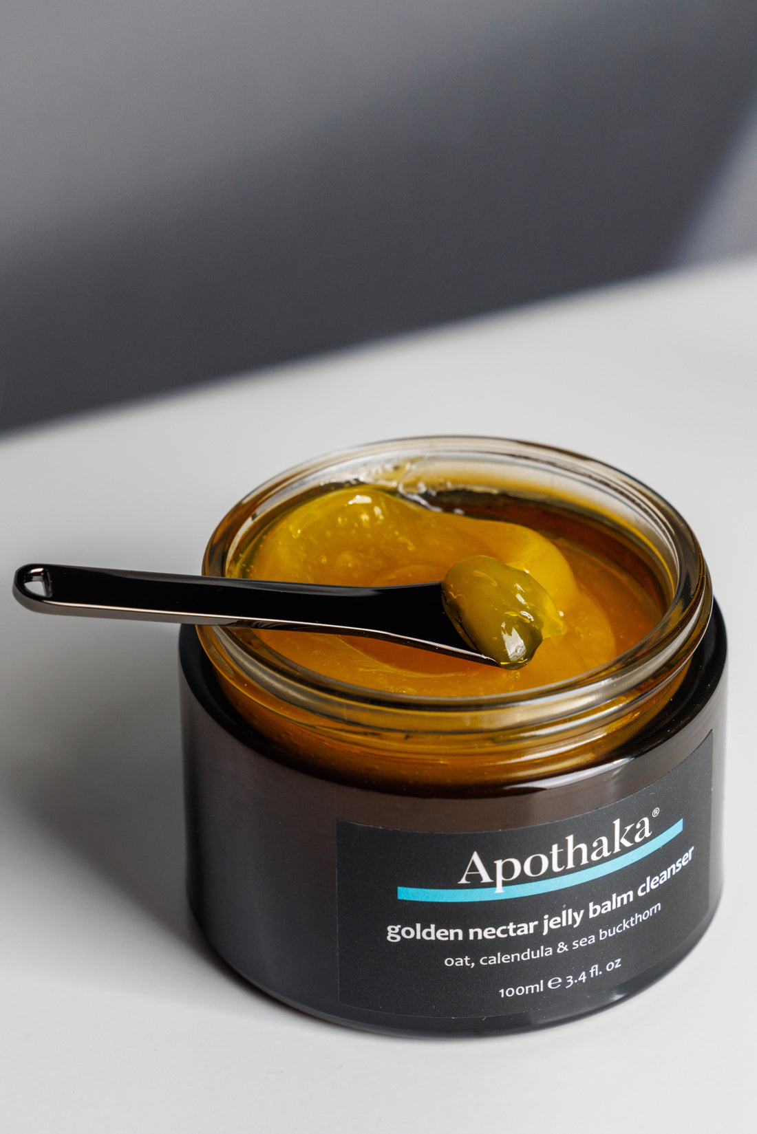 Apothaka golden nectar jelly balm cleanser texture with spatula, showing a vibrant orange gelled oil texture in an open jar